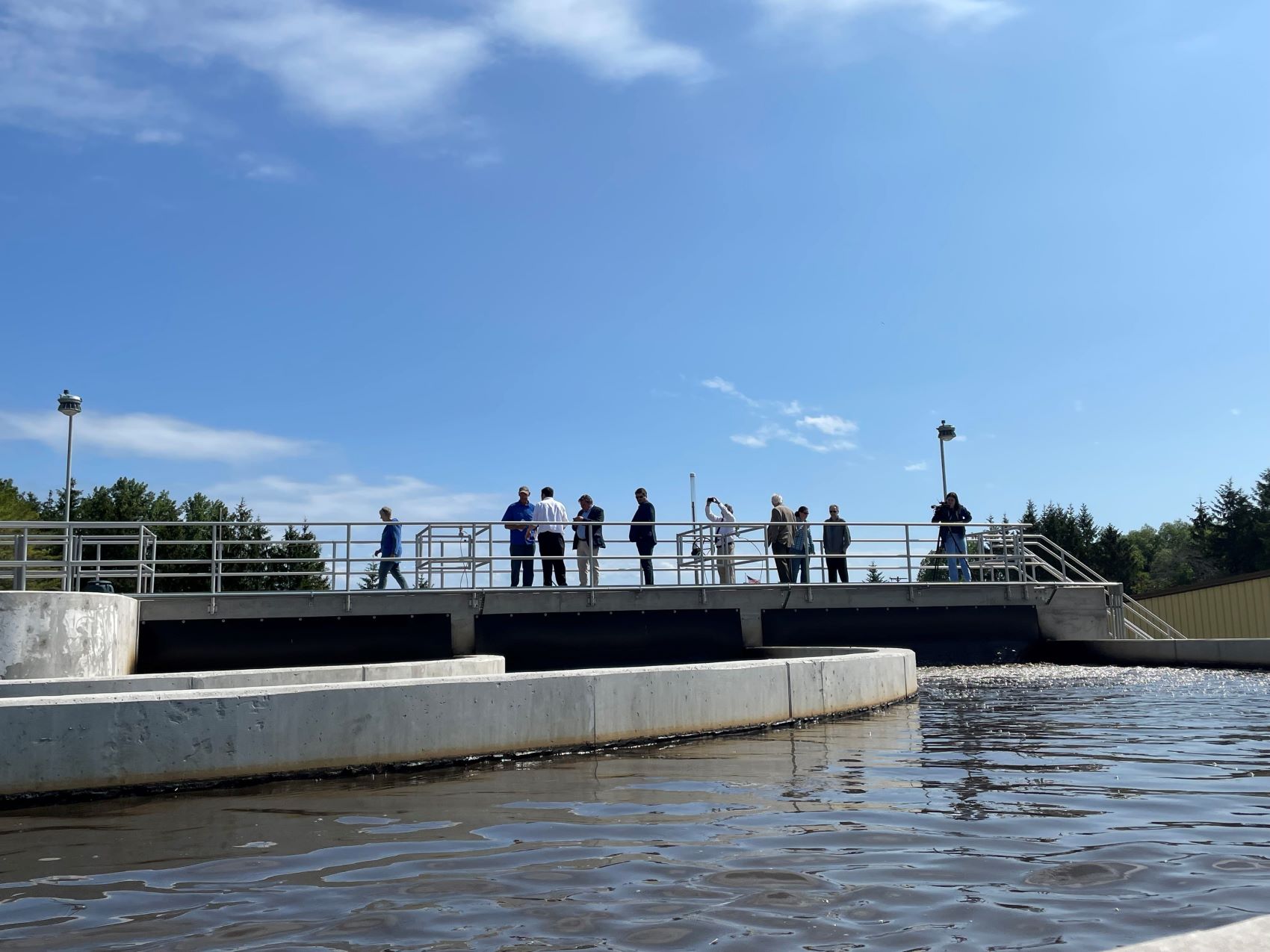 people standing on walkover above wastewater treatment lagoon